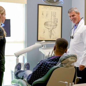 A dentist consulting a male patient while a woman stands nearby in a dental clinic.