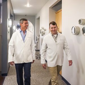 Two men in white lab coats walking down a hallway in a medical facility.